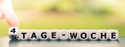 Hand turns a dice and changes the German  expression "5 tage woche" ("5 day week" in English) to "4 tage woche" ("4 day week" in English).